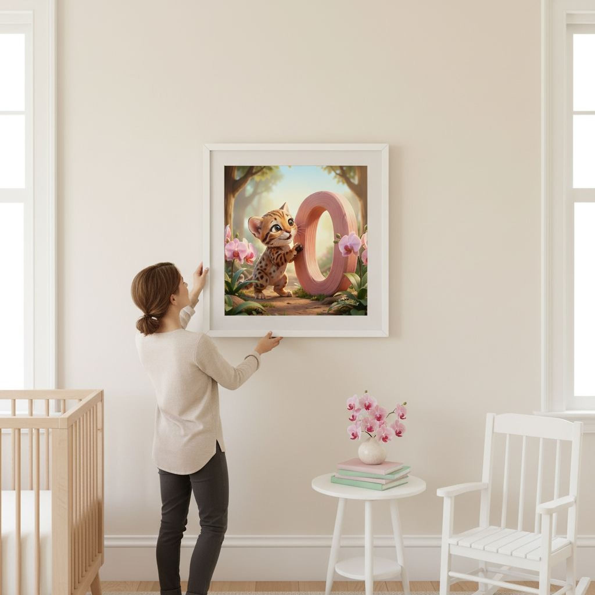 A woman hangs a framed artwork on a wall in a room with a crib, a small table with flowers, and a rocking chair.