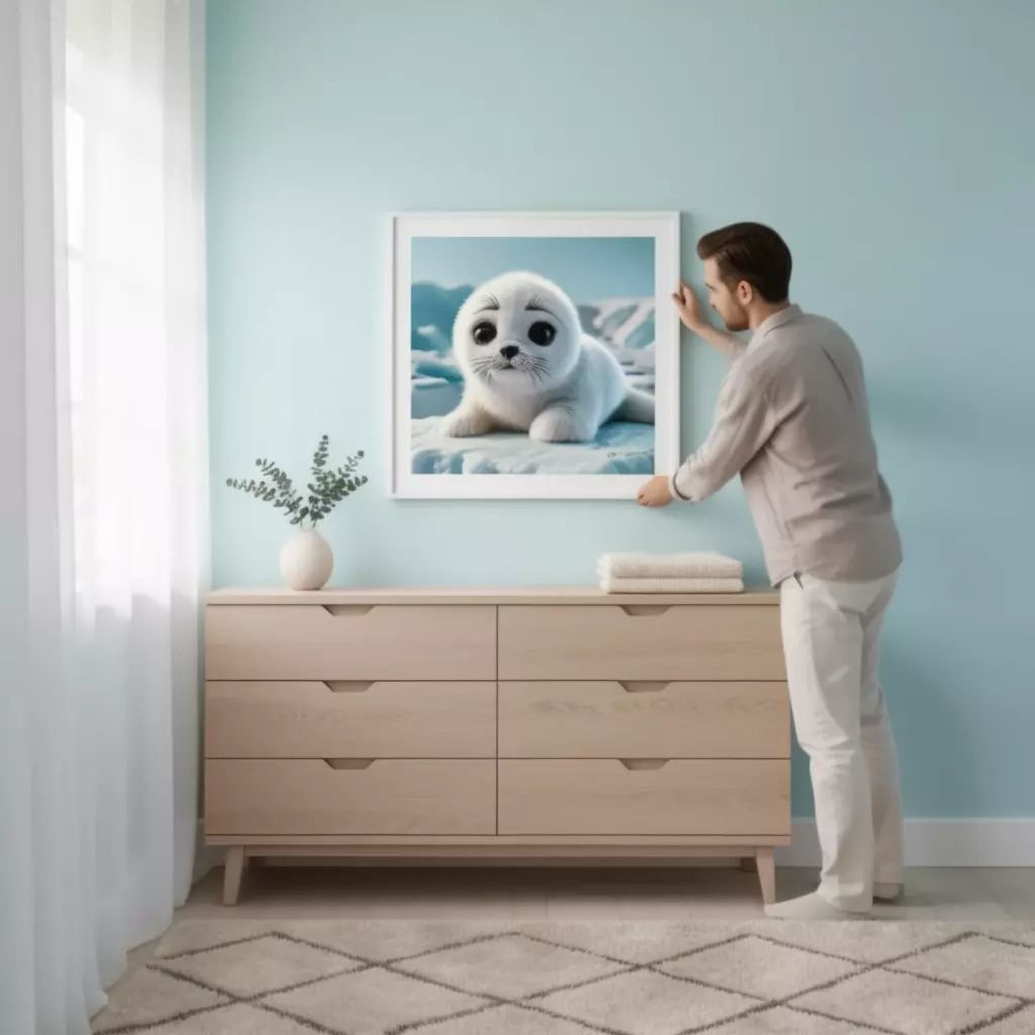 A man is standing in a room, hanging a framed picture of a seal on the wall above a wooden dresser.